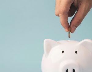 Jemand steckt eine Münze in den Schlitz eines weißen Sparschweins.