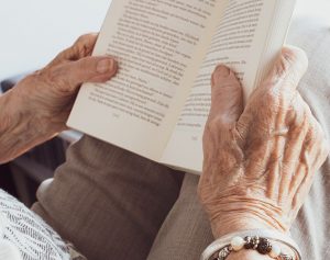 Eine alte Frau hält ein aufgeschlagenes Buch mit beiden Händen vor sich.