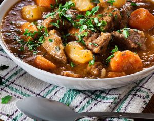 Artikel-Header: Ein Teller mit einem deftigen Eintopf aus Kartoffeln, Rindfleisch und Karotten