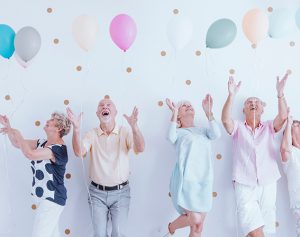 Artikel-Header: Eine Gruppe älterer Menschen schaut lachend bunten Liftballonen nach, die in die Luft steigen.