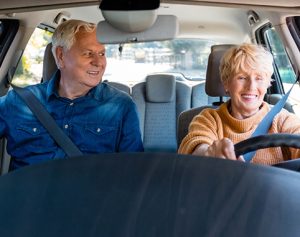 Header-Artikel: Ein älteres Paar sitzt im Auto, die Frau fährt und beide lächeln.