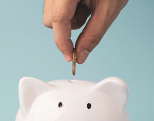 Header-Artikel: Jemand gibt eine Münze in den Schlitz eines Sparschweins.