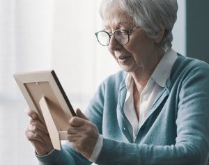 Header_Artikel: ältere Frau schaut betrübt auf das Foto eines Verstorbenen