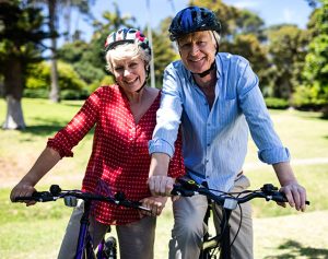 Ein älteres Paar sitzt auf ihren Fahrrädern und lächelt in die Kamera.