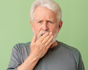 Header-Artikel: Älterer Mann hält sich die Hand vor den Mund und verzieht sein Gesicht.