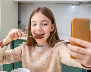Header-Artikel: Kind führt einen Löffel mit Pulverkaffee zum Mund und filmt sich dabei mit seinem Handy.