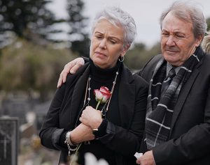 Trauernde Menschen stehen in schwarz gekleidet vor einem Grab.