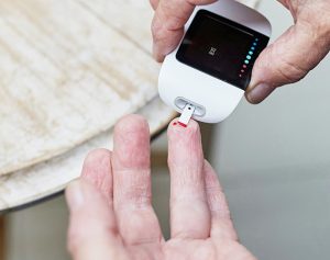 Eine ältere Person misst den Zuckergehalt in einem Blutstropfen mit einem Zuckermessgerät.