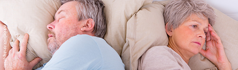 Ein älteres Paar liegt in einem Bett. Der Mann schläft. Die Frau ist wach und schaut besorgt. 